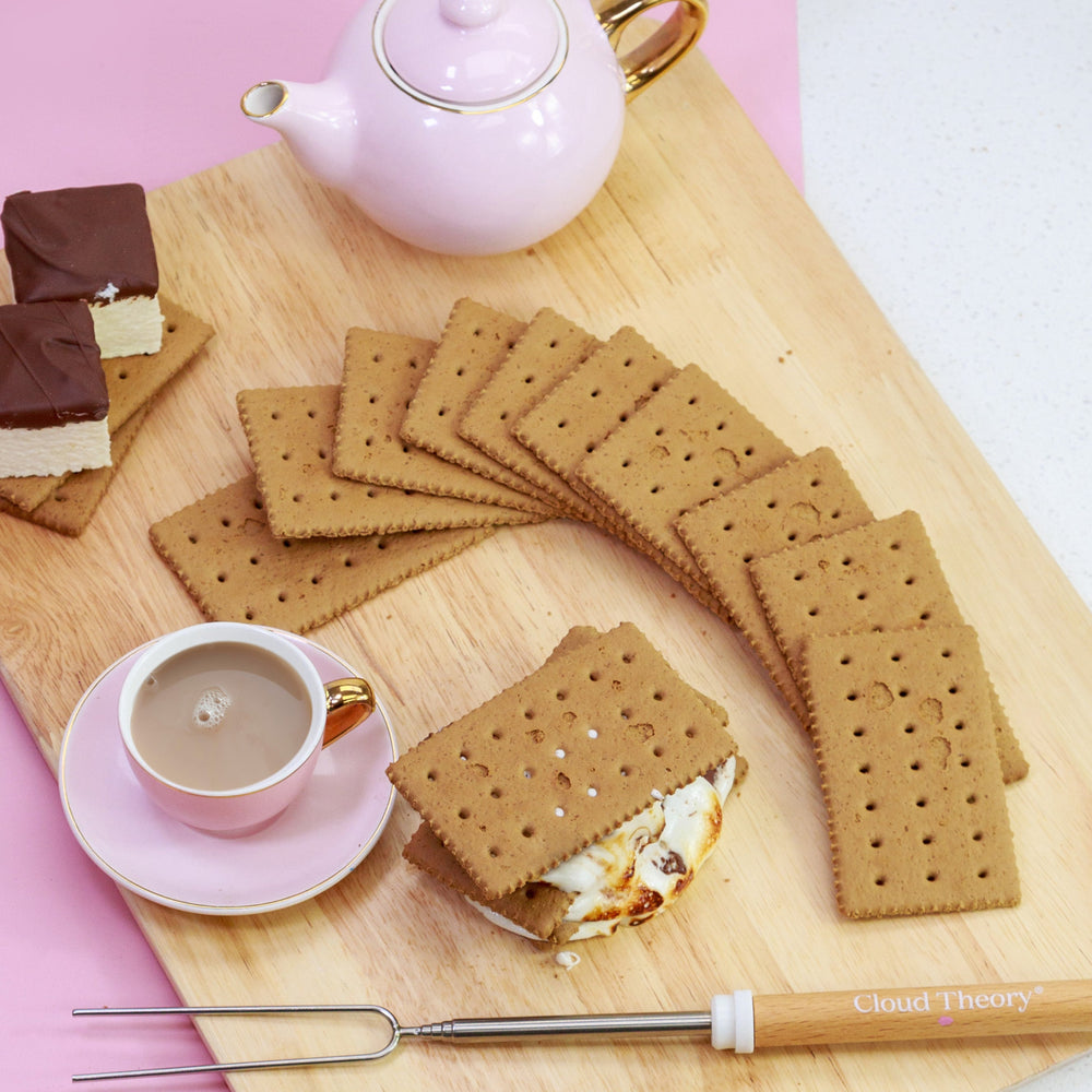 Golden honey-flavoured graham crackers stacked neatly next to marshmallows and chocolate, perfect for s’mores, cheesecake bases, and baking.