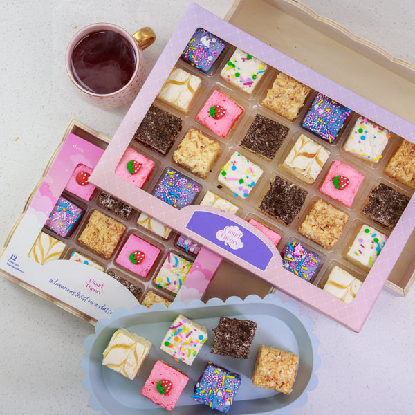 Assorted small desserts in a box with a cup of tea on a light surface