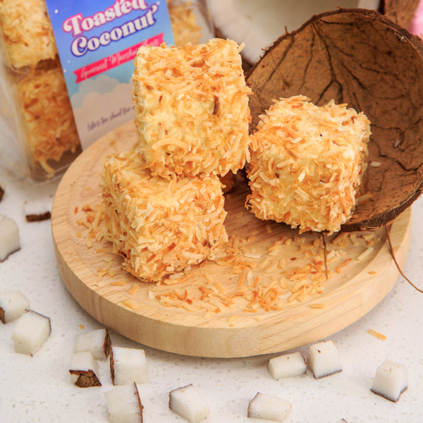Toastet Coconut treats on a wooden board with a coconut and marshmallows in the background.