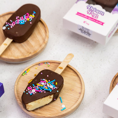 Chocolate-dipped ice cream bars with sprinkles on wooden plates, with a box of Dream Pop in the background.
