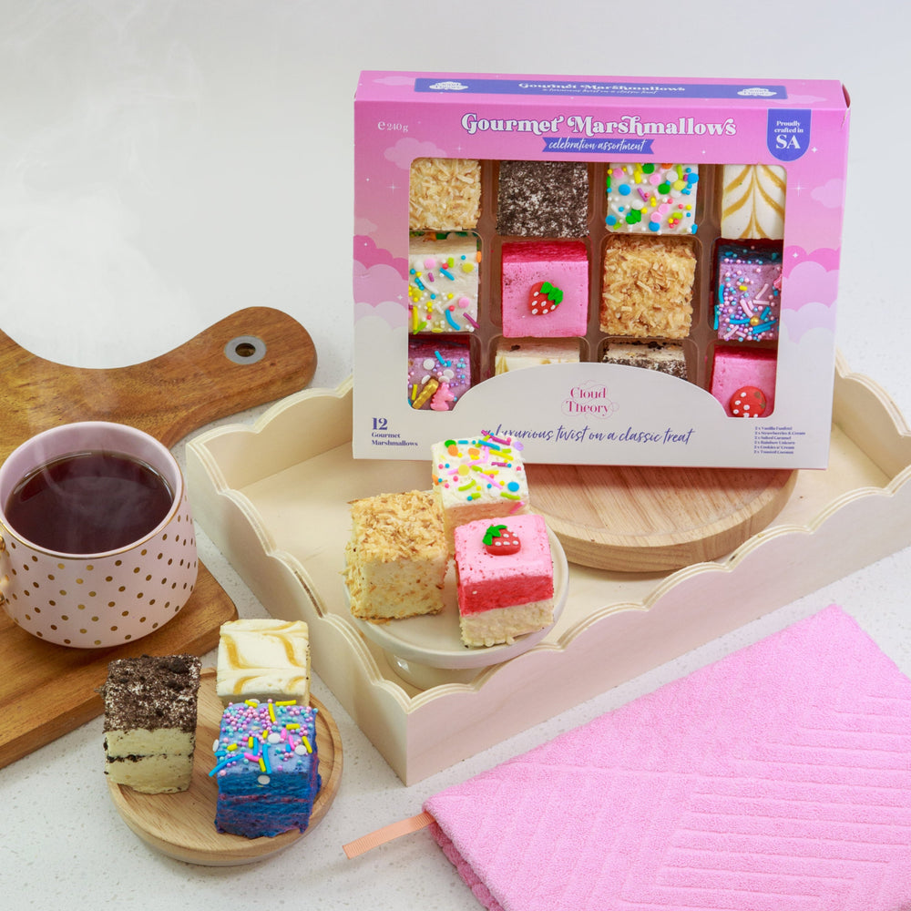 Assorted marshmallow treats on a tray with a mug of tea and a pink pouch.