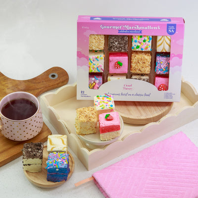 Assorted marshmallow treats on a tray with a mug of tea and a pink pouch.