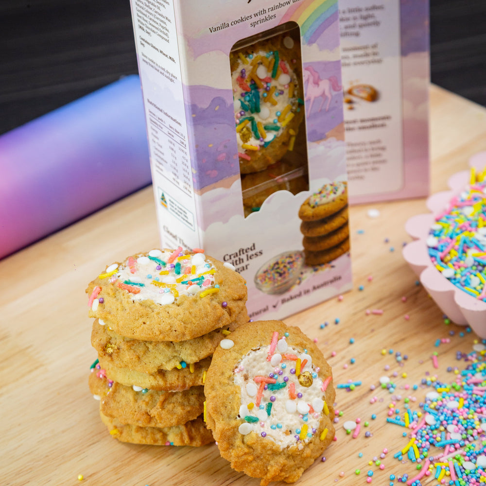 Stack of cookies with rainbow sprinkles on a wooden board, next to a box labeled 'Rainbow Joy' from Cloud Theory.