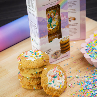 Stack of cookies with rainbow sprinkles on a wooden board, next to a box labeled 'Rainbow Joy' from Cloud Theory.