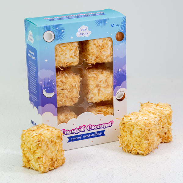 Box of roasted coconut marshmallows with two marshmallows in front on a white background